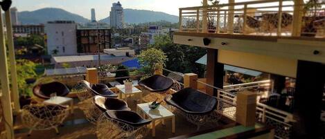Une terrasse sur le toit, aménagée avec des meubles en osier et un espace bar, offrant une vue panoramique sur la ville, avec des montagnes en toile de fond.