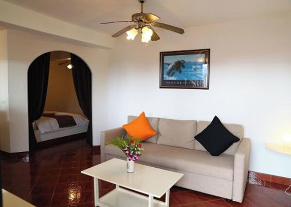 A living room with a sofa, a coffee table, a ceiling fan, and a framed picture on the wall. - Swiss Villas Panoramic – Hillside Beach View (Patong)