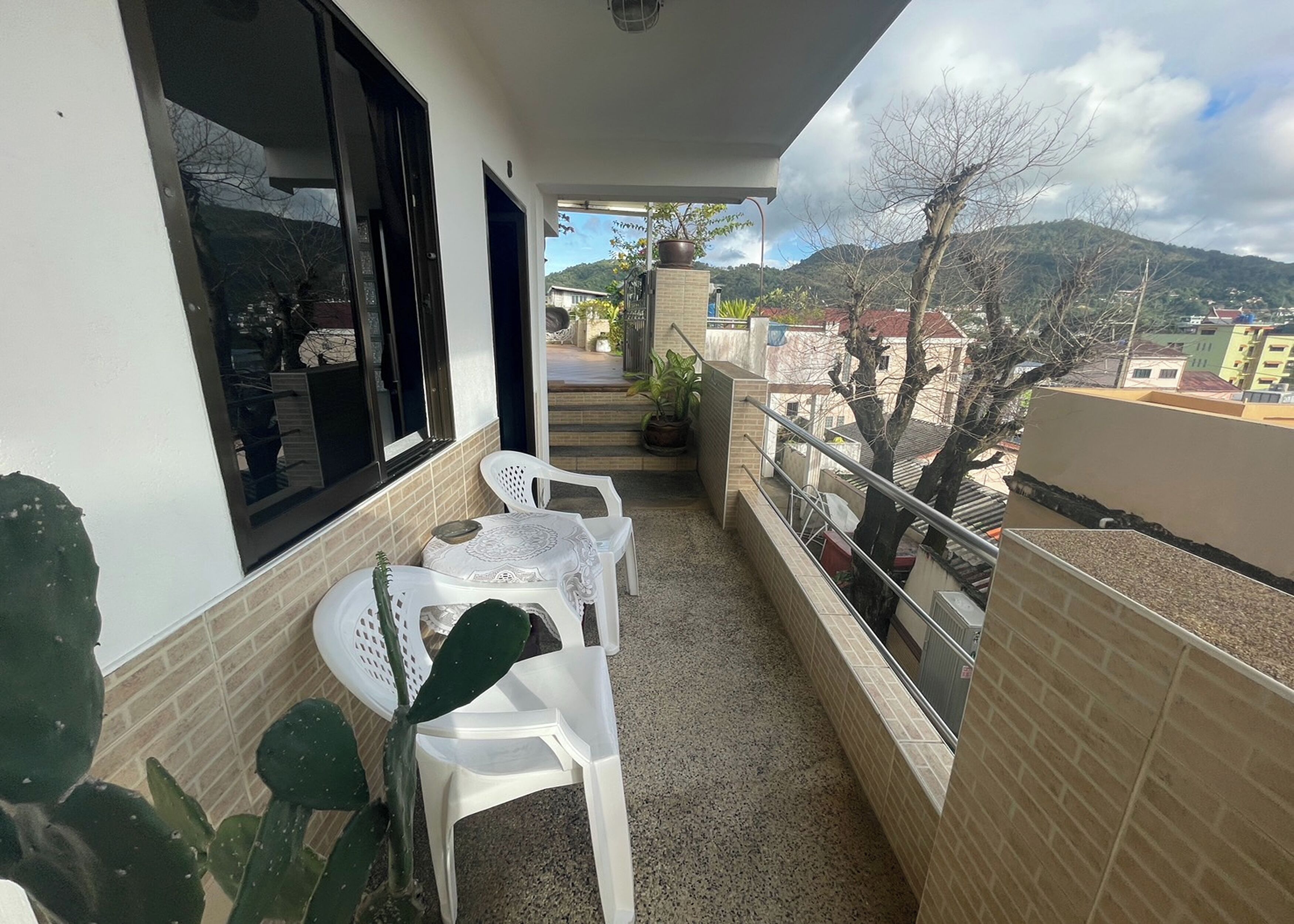 A balcony with a table and chairs, a potted plant, and a view of a mountain and buildings.