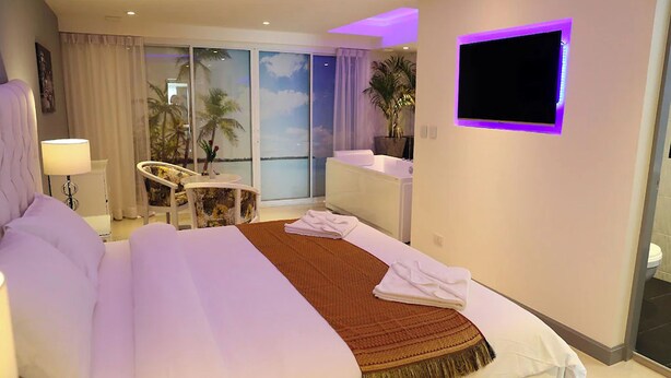 Habitación de hotel con una cama grande, televisor montado en la pared, balcón con vistas y un escritorio con silla.