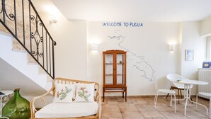 A room with a wicker sofa, a wooden cabinet, and a white table with chairs. A map on the wall reads "WELCOME TO PUGLIA." - Bella Bari rooms (Bari)