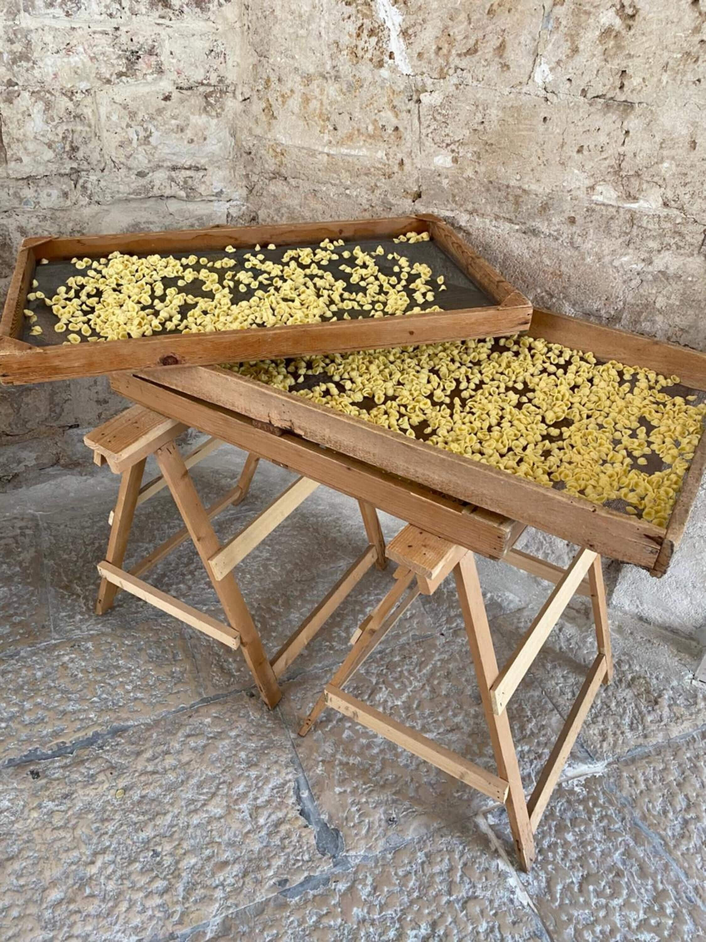 Un tamiz de madera con granos amarillos sobre un suelo de piedra.