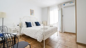 A bedroom with a bed, a chair, a nightstand, a lamp, and an air conditioning unit. - Bella Bari rooms (Bari)