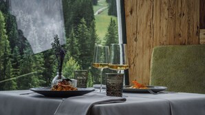 Una mesa de comedor con un plato de comida, dos copas de vino y un florero con flores.