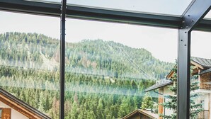 Una pareja en una piscina infinita cubierta de cristal con vistas a una montaña boscosa.