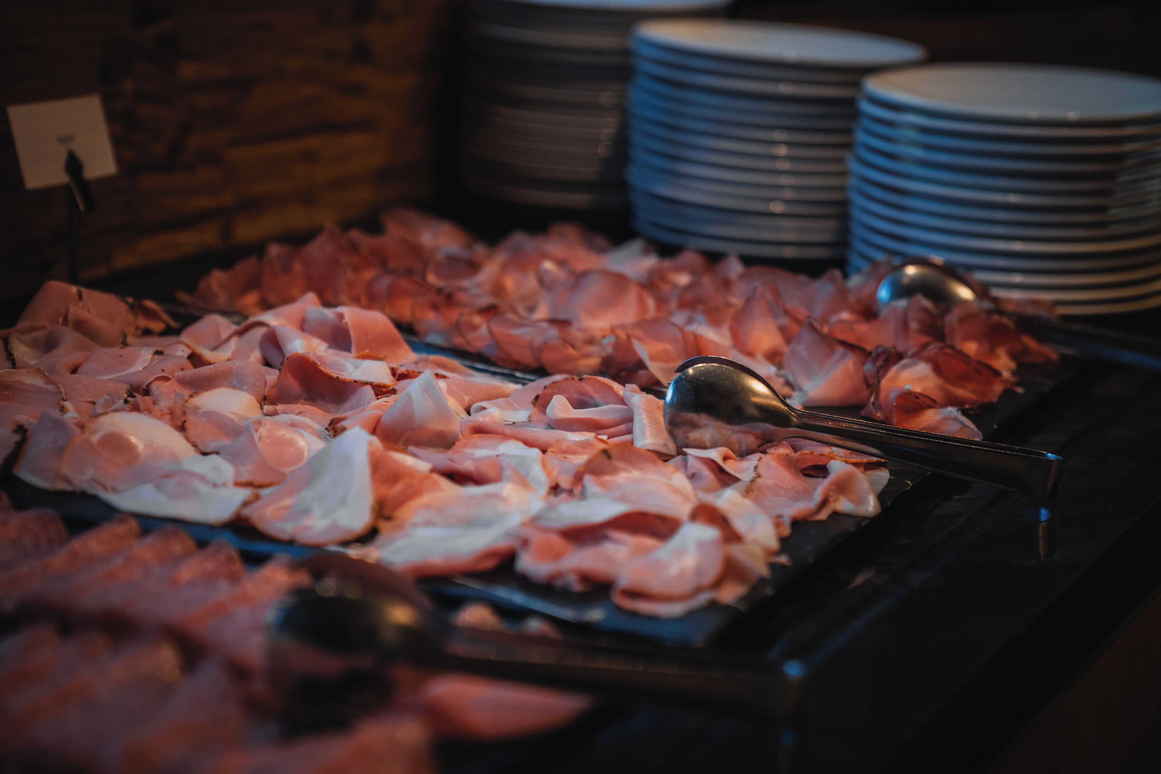 Un buffet con diversi tipi di carne e una pila di piatti sullo sfondo.