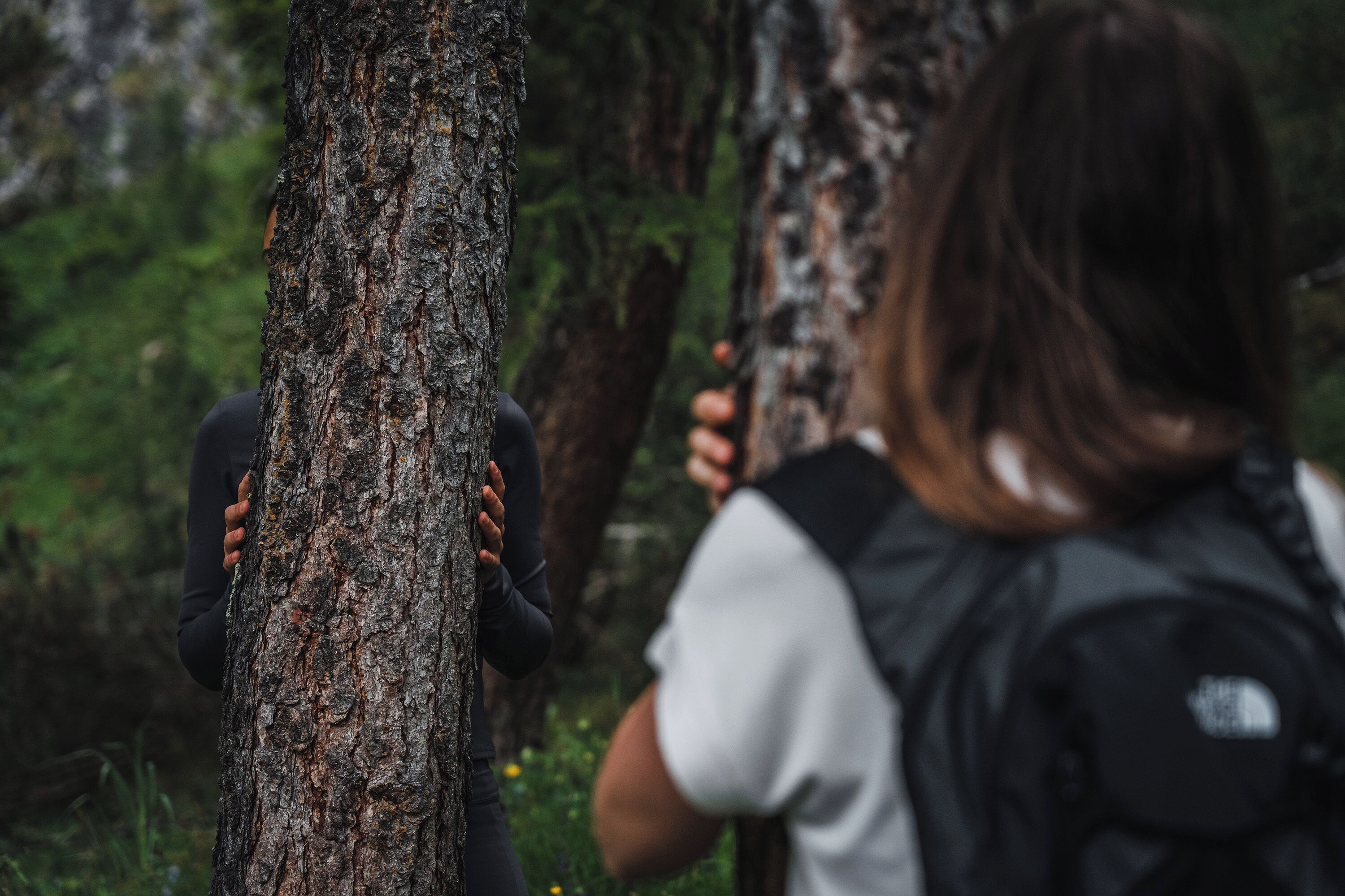 A person with a backpack leaning against a tree in a forested area.