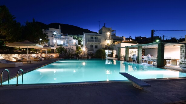 A swimming pool with lounge chairs and umbrellas, surrounded by buildings with stone pillars and a mountainous backdrop. - Nefeli Villas (Skiros)