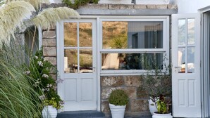 A stone wall with a window and door, surrounded by potted plants. - Nefeli Villas (Skiros)