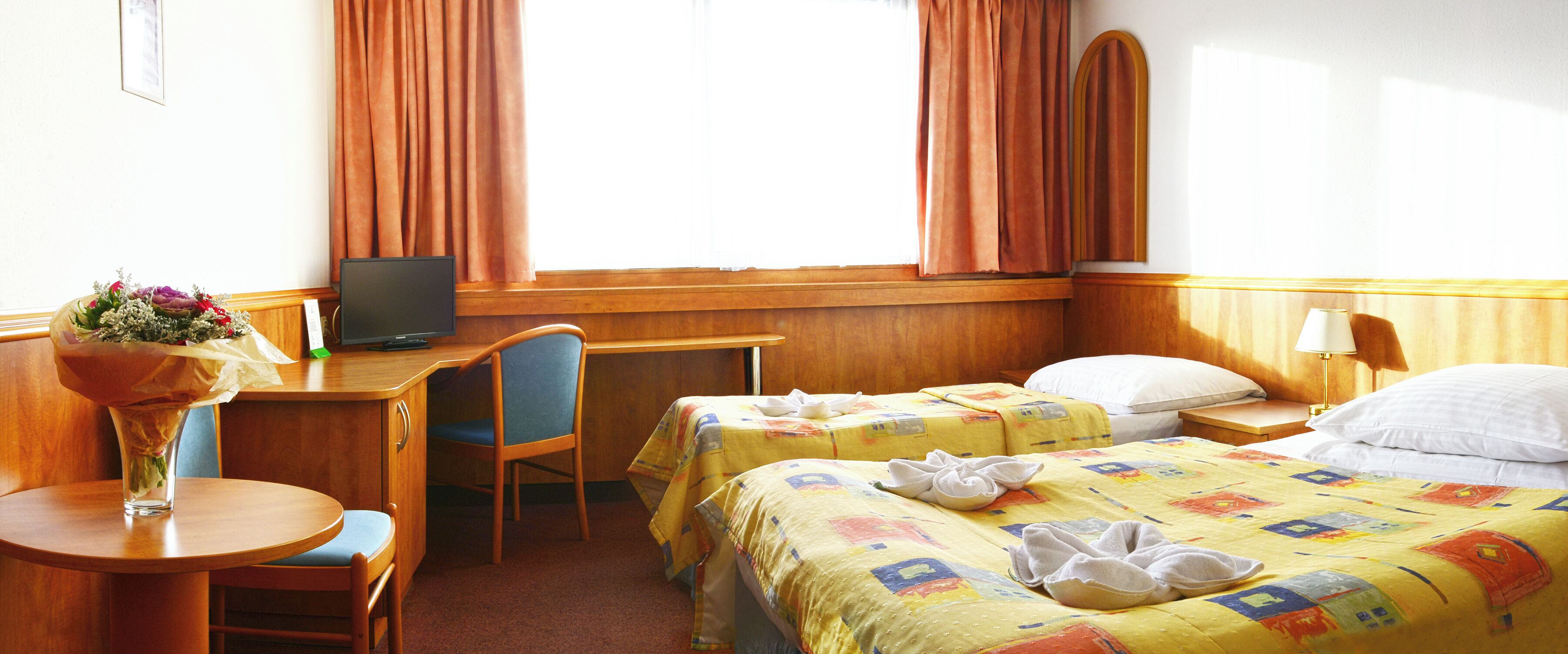 Habitación de hotel con dos camas, un escritorio, una silla, un televisor y una ventana con cortinas.