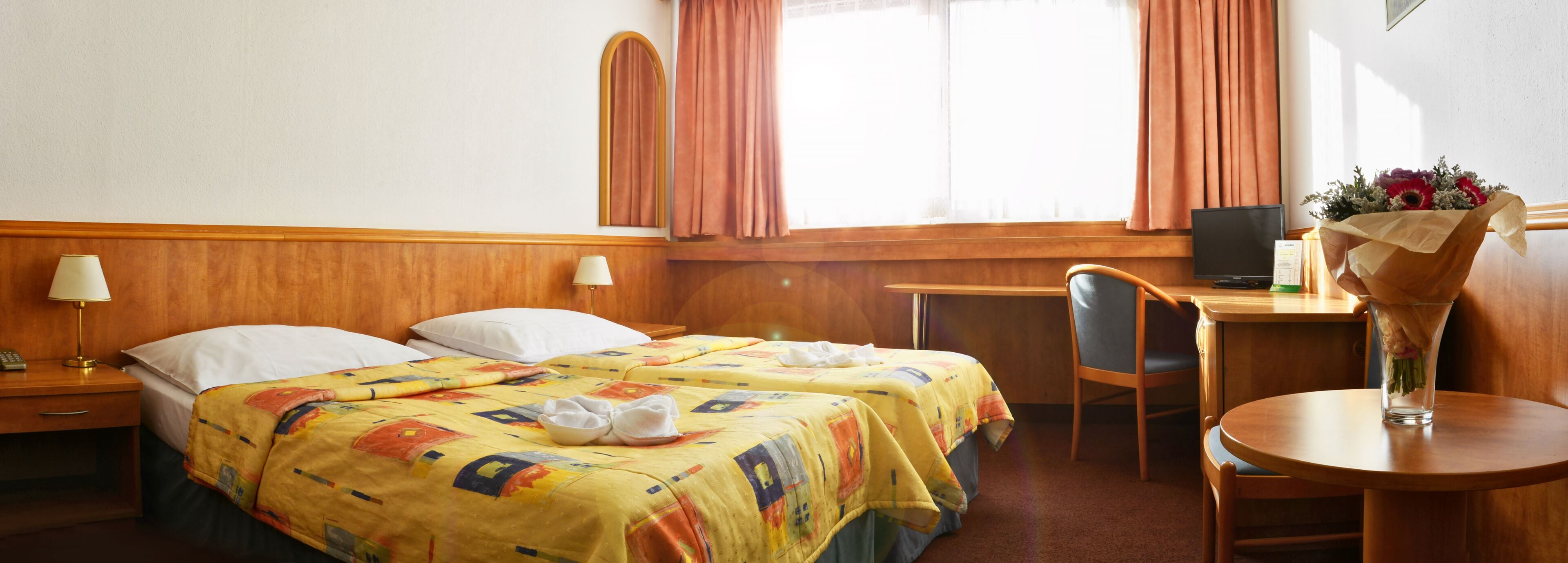 Habitación de hotel con dos camas, un escritorio, una silla, un televisor y un florero con flores.
