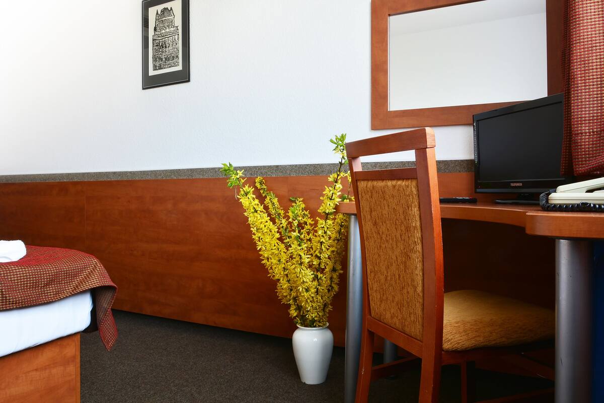 A hotel room with a bed, a desk with a computer, a chair, and a potted plant.