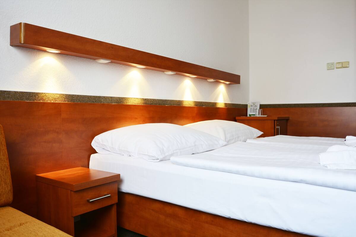 A hotel room with a wooden headboard, two beds, a nightstand, and a wall-mounted light fixture.