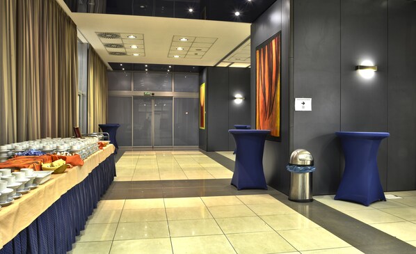 A modern hotel lobby with a buffet table, a reception desk, and a large painting on the wall.