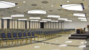 Une salle de conférence avec des rangées de chaises bleues et une scène sur laquelle se trouve un pupitre.