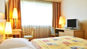Une chambre d’hôtel comprenant un lit, un bureau avec une télévision, deux chaises et une lampe.