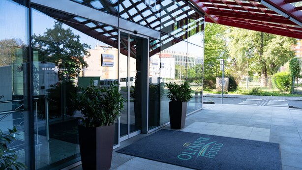 L’entrée d’un hôtel, avec une façade en verre, un auvent rouge et un paillasson portant le nom de l’hôtel.