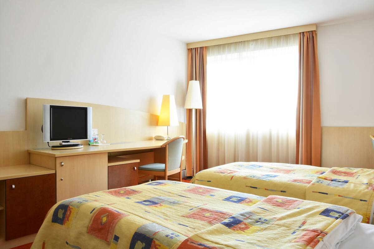 A hotel room with two beds, a desk with a computer, a chair, and a lamp.