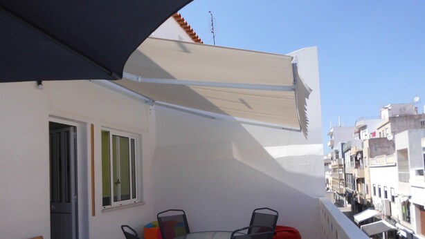 A balcony with a table and chairs, a red bean bag, and a white awning. - Alameda Hostel (Portimão)