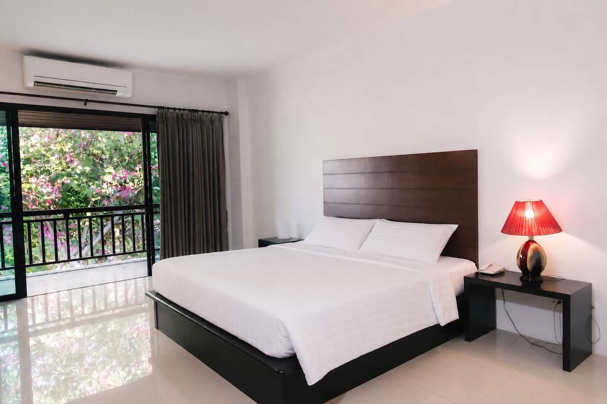 Habitación de hotel con cama, mesita de noche con lámpara y vista a zonas verdes por la ventana.