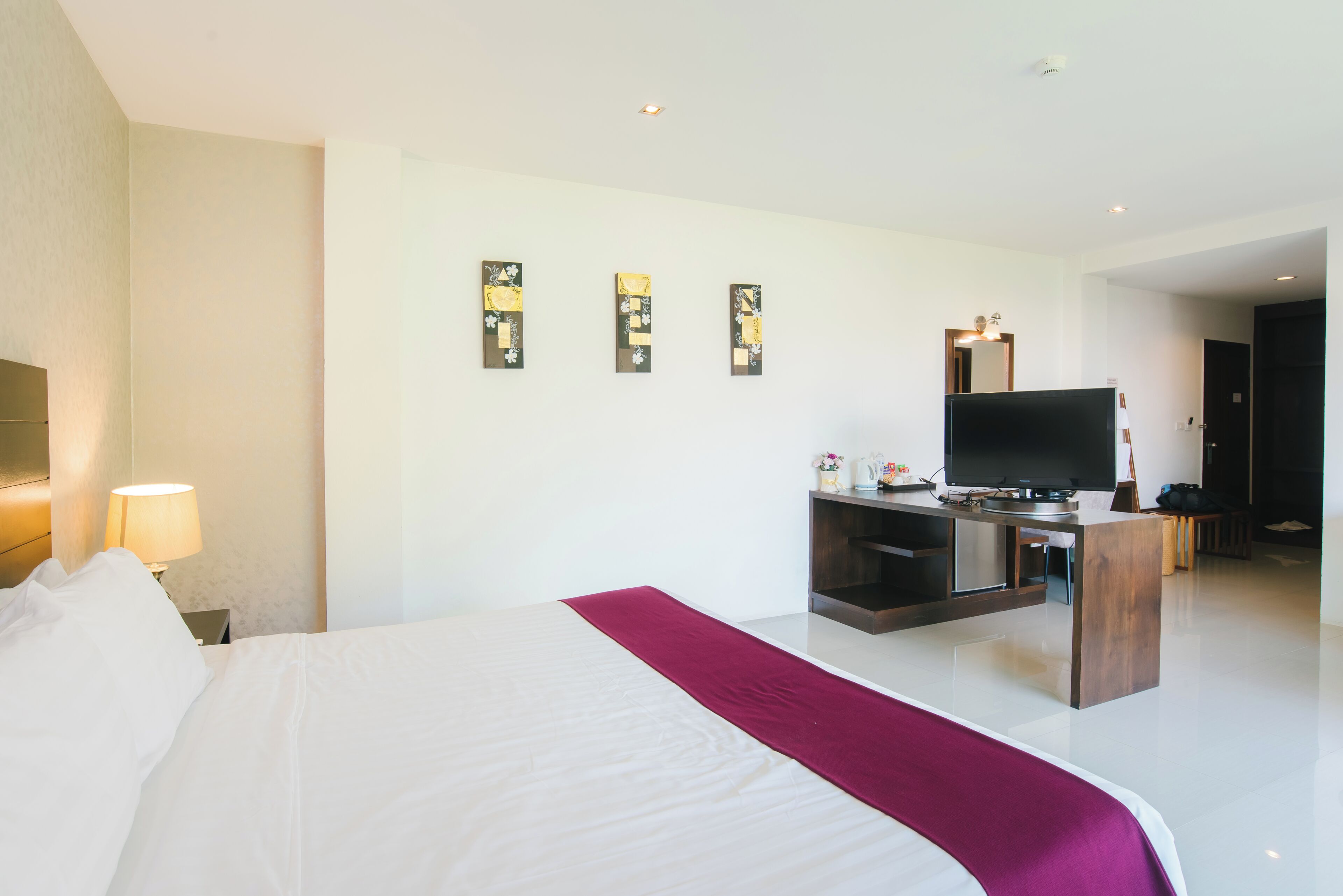 A hotel room with a bed, a TV, a desk, and artwork on the wall.