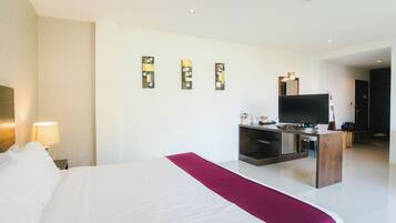 A hotel room with a bed, a TV, a desk, and artwork on the wall.