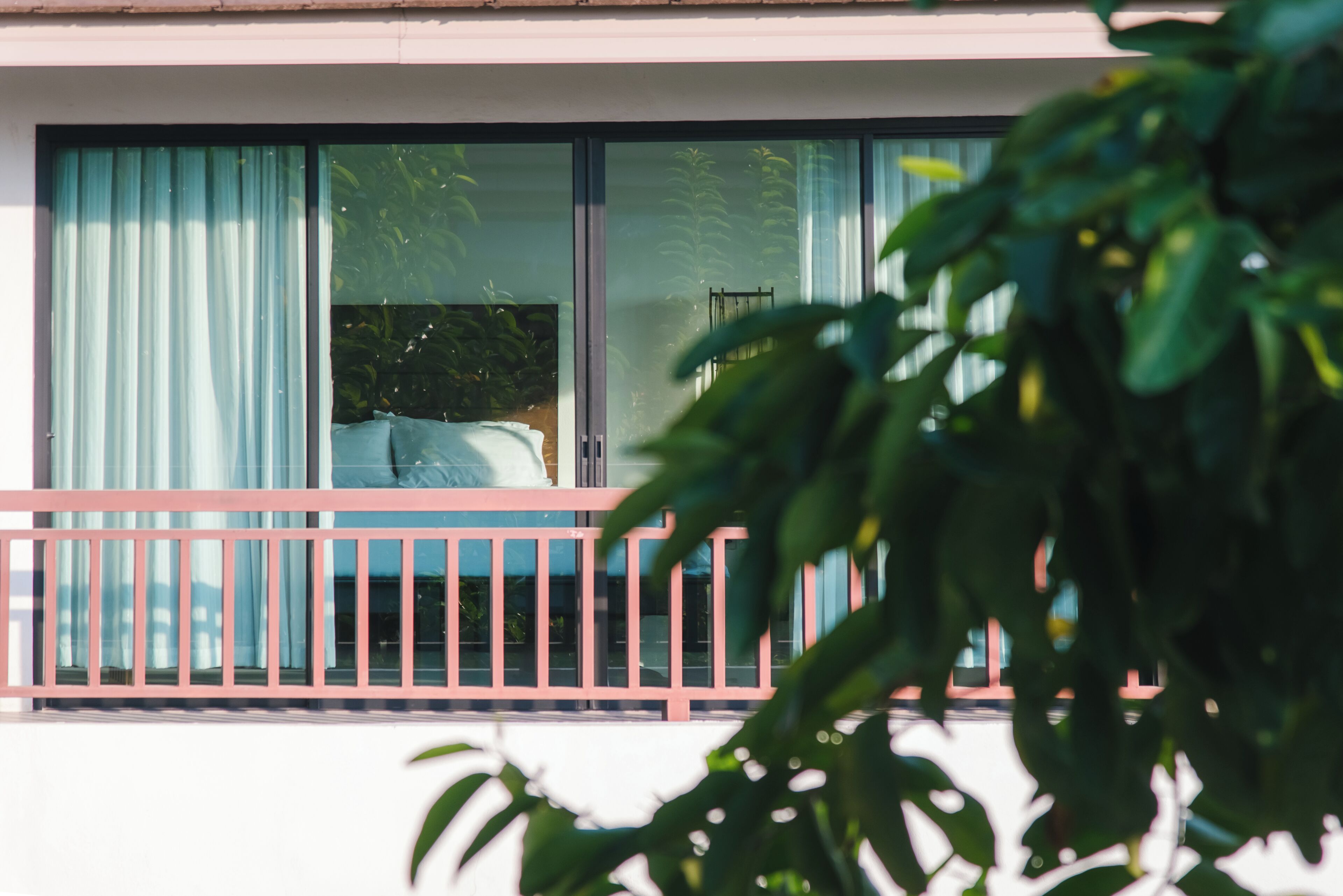 Un balcón con barandilla rosa, una cama y una ventana con cortinas.