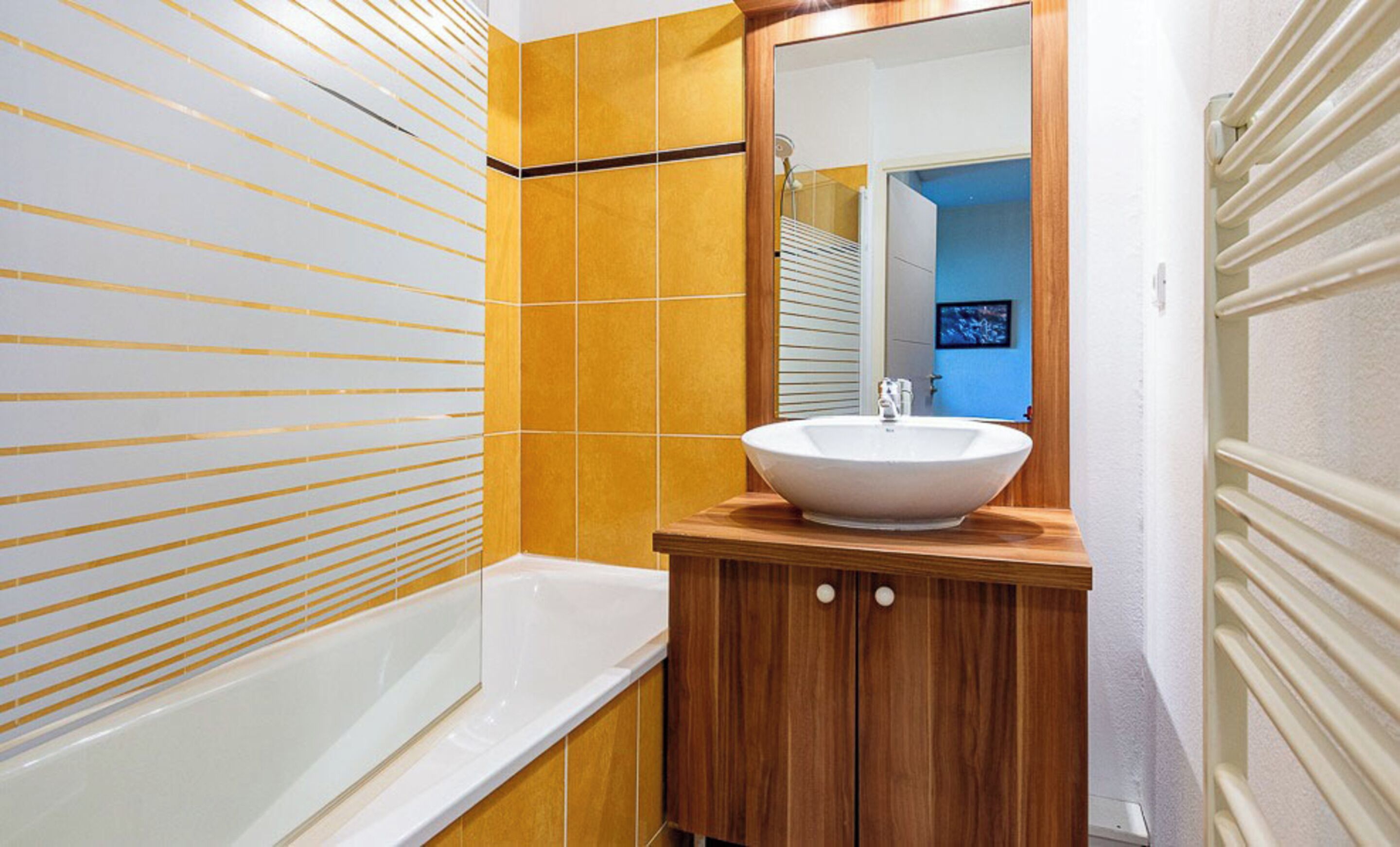 A bathroom with a bathtub, a wooden vanity with a sink, and a mirror above the vanity.