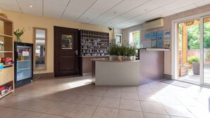 Un espace d’accueil doté d’un sol carrelé, d’un comptoir de réception, d’un réfrigérateur et d’une porte donnant sur un jardin.