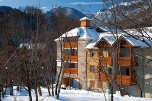 A multi-story building with balconies, surrounded by snow-covered trees and mountains. - Résidence Vacancéole Les Chalets d'Ax (Ax-les-Thermes)