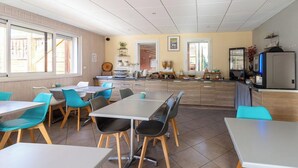 A dining area with tables and chairs, a kitchen area with appliances, and a view of the outside through large windows.