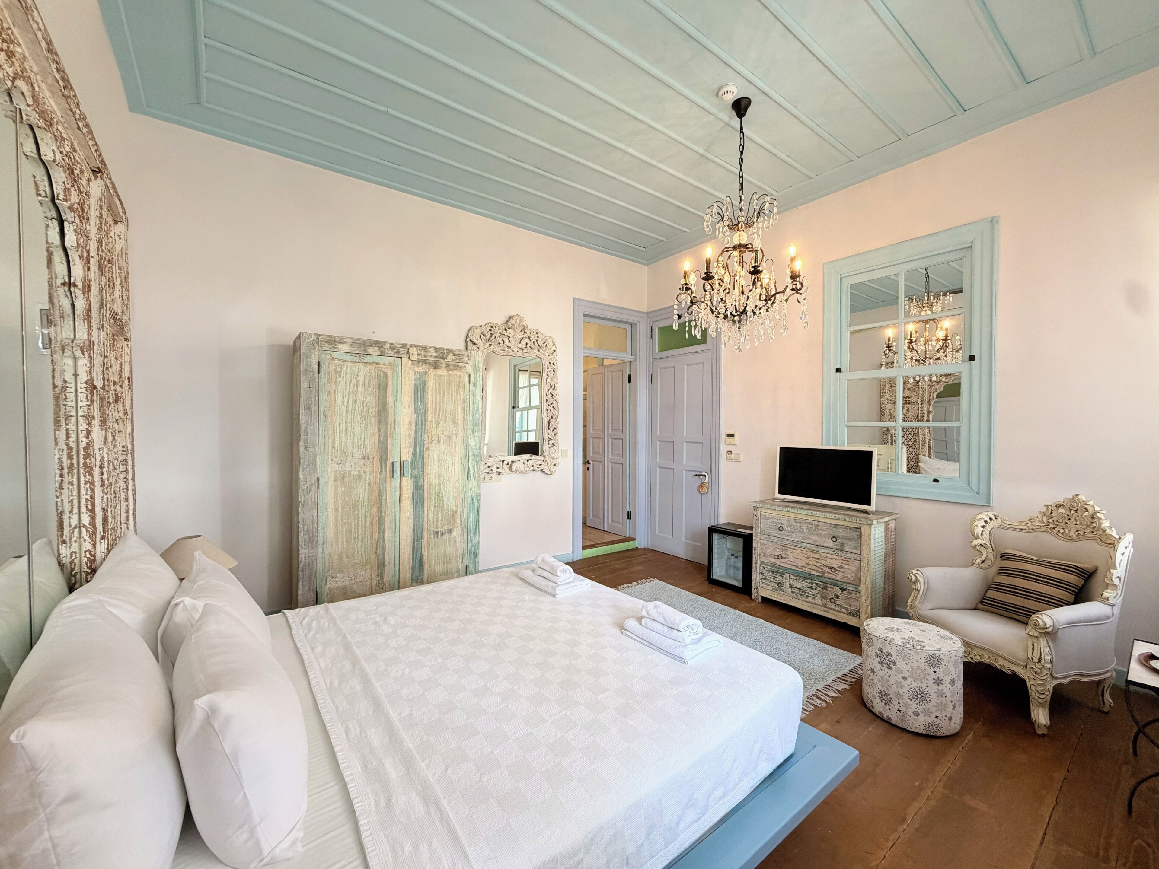 A bedroom with a bed, dresser, chair, and a chandelier.