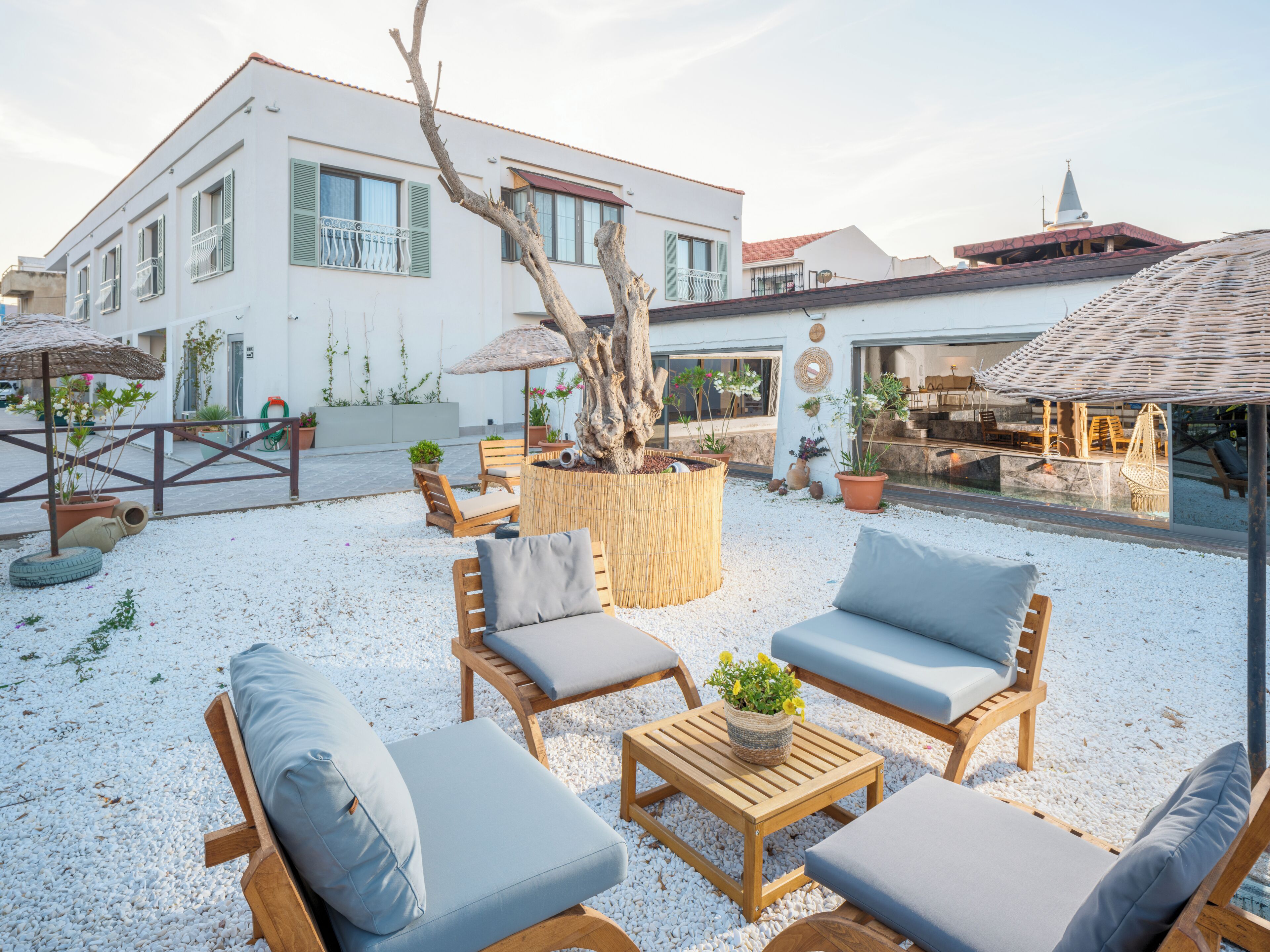 Un patio con mobiliario exterior, una jardinera con árbol y un edificio con balcón.