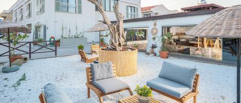 Un patio con mobiliario exterior, una jardinera con árbol y un edificio con balcón.