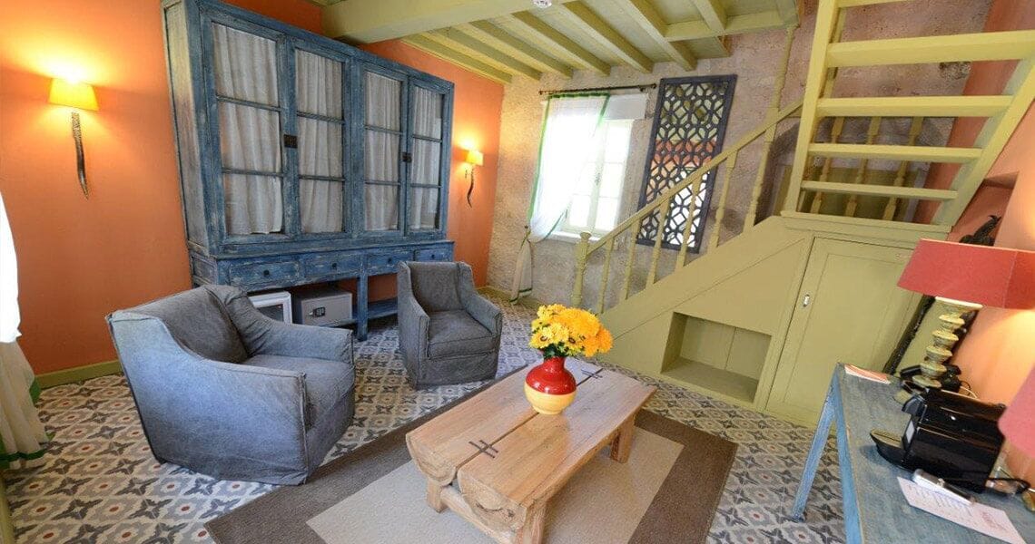 A cozy room with a blue cabinet, two grey armchairs, a wooden coffee table, and a staircase with a wooden railing.