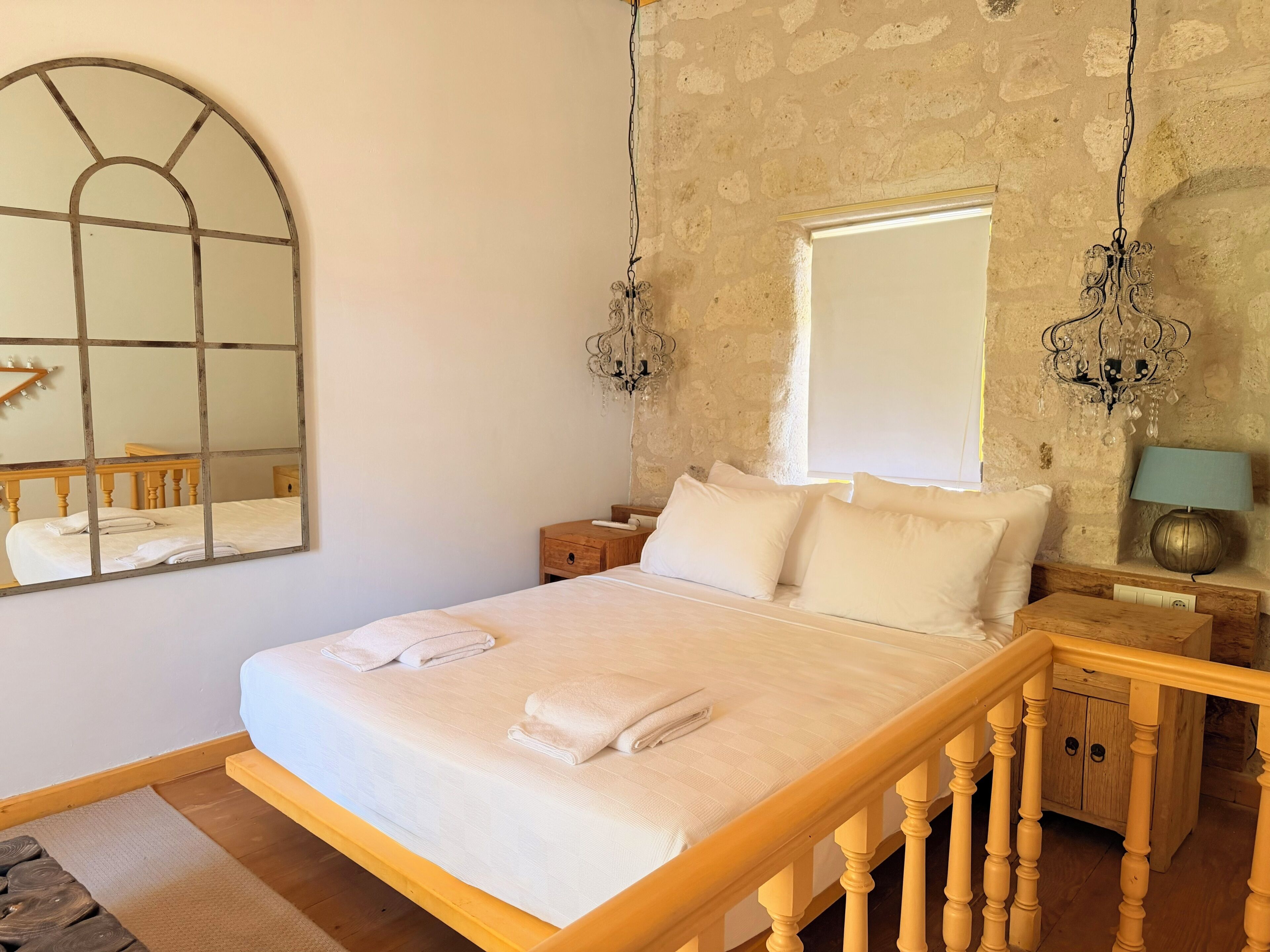 A bedroom with a bed, wooden headboard, nightstands, a mirror, and a chandelier.