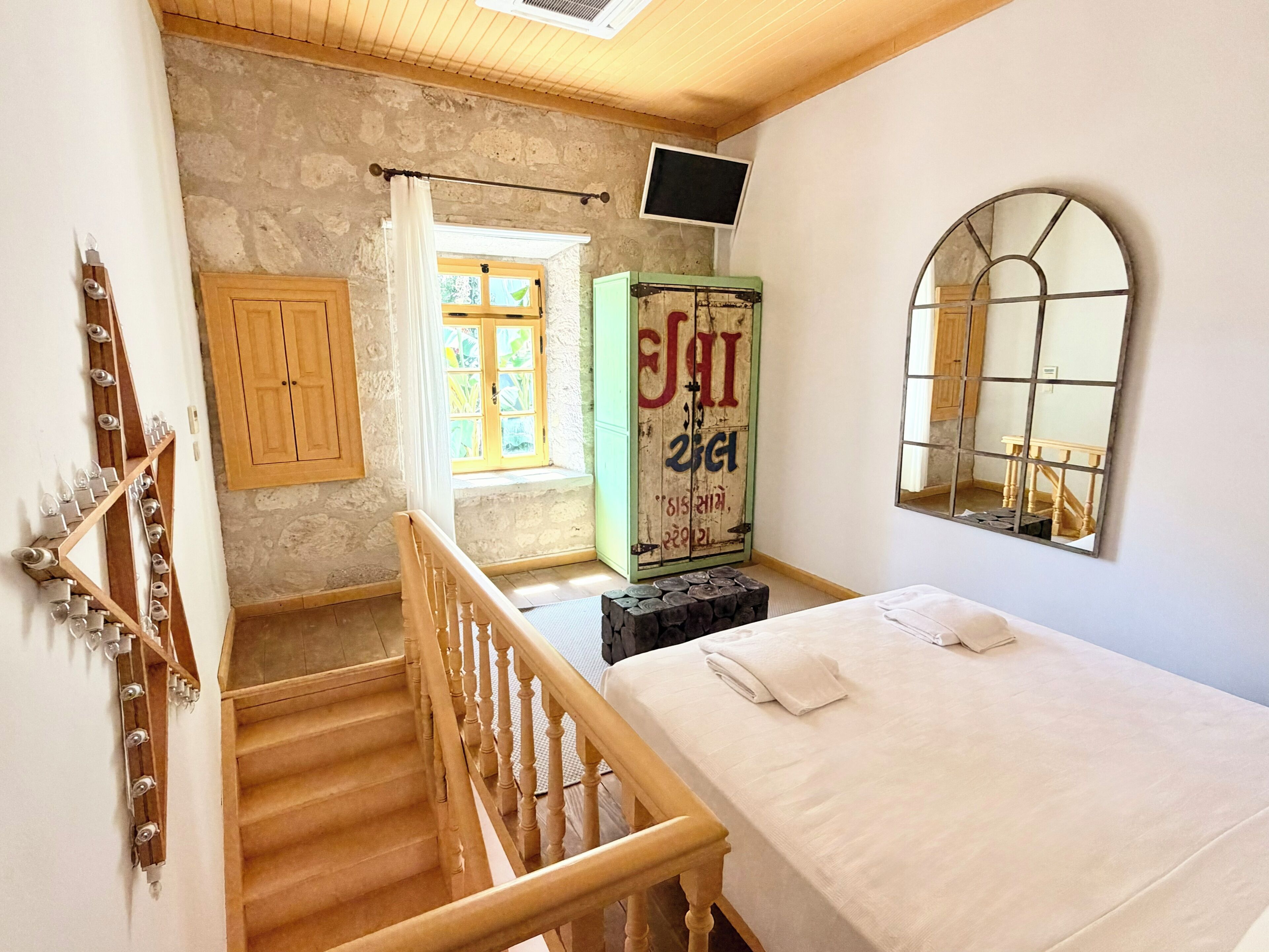 Una camera da letto con un letto, una scala in legno, un armadio, una finestra e uno specchio.
