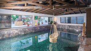Una piscina interior con agua cristalina, vigas de madera y plantas en macetas.