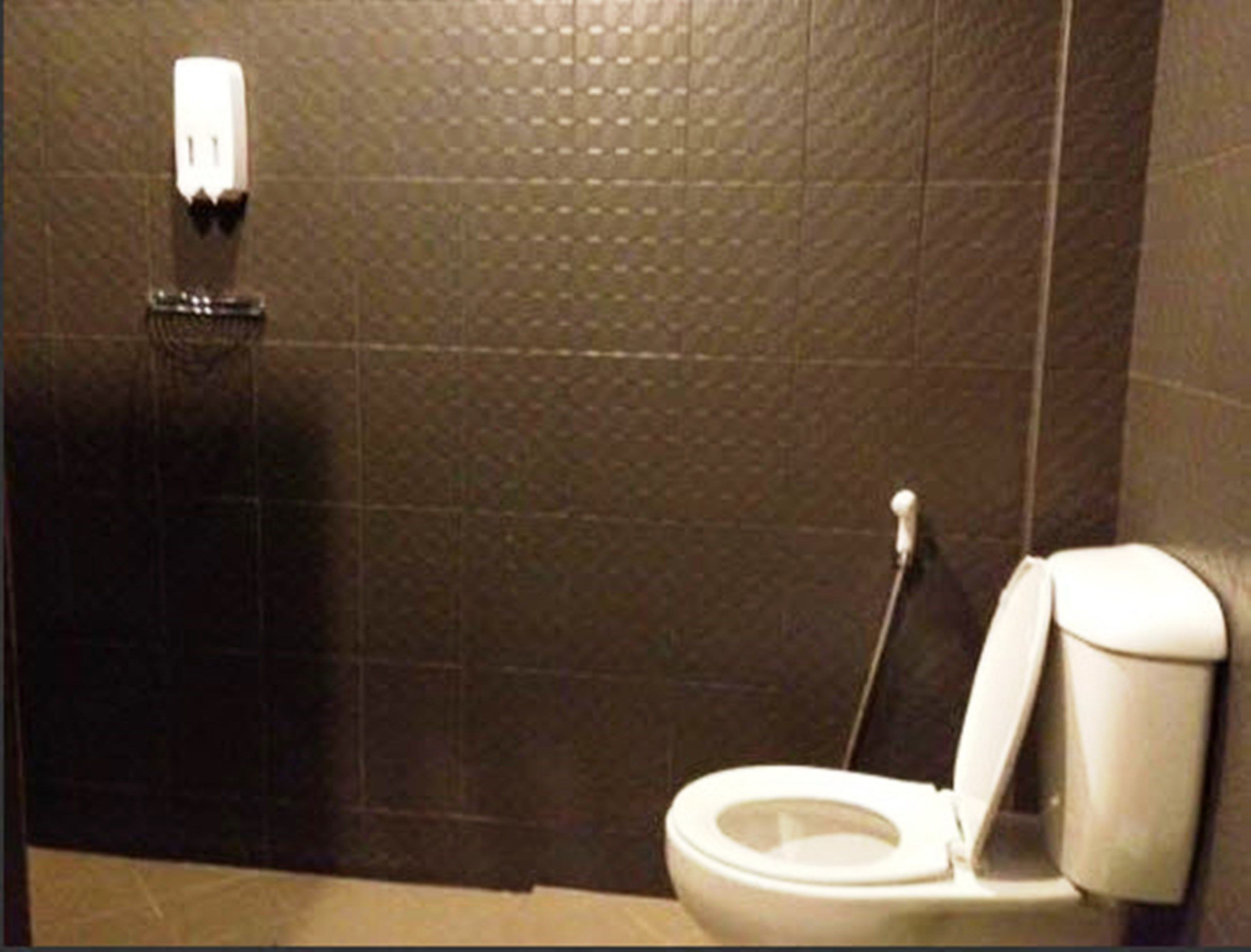Ein Badezimmer mit Toilette, einem Händetrockner und einem an der Wand befestigten Seifenspender.