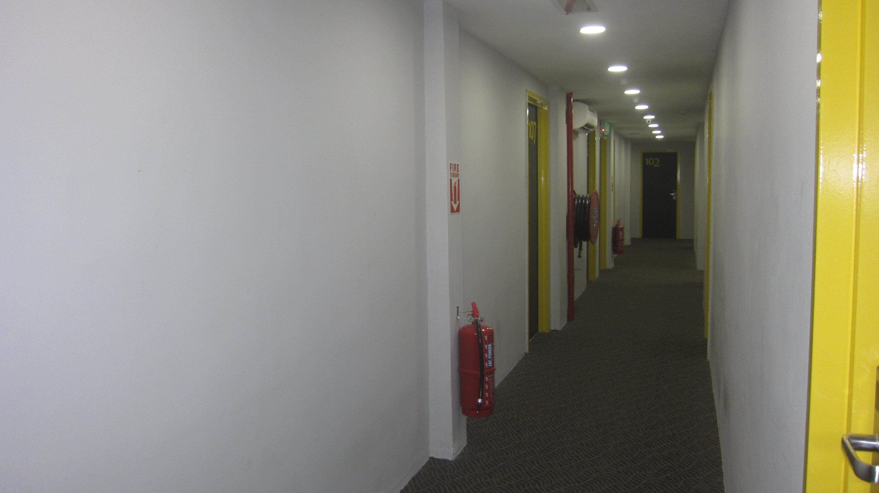 A hotel corridor with doors, a fire extinguisher, and a fire exit sign.