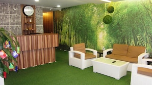 A reception area with a wooden desk, white wicker chairs, and a green artificial forest wall. - Dream Garden Hotel (Klang)