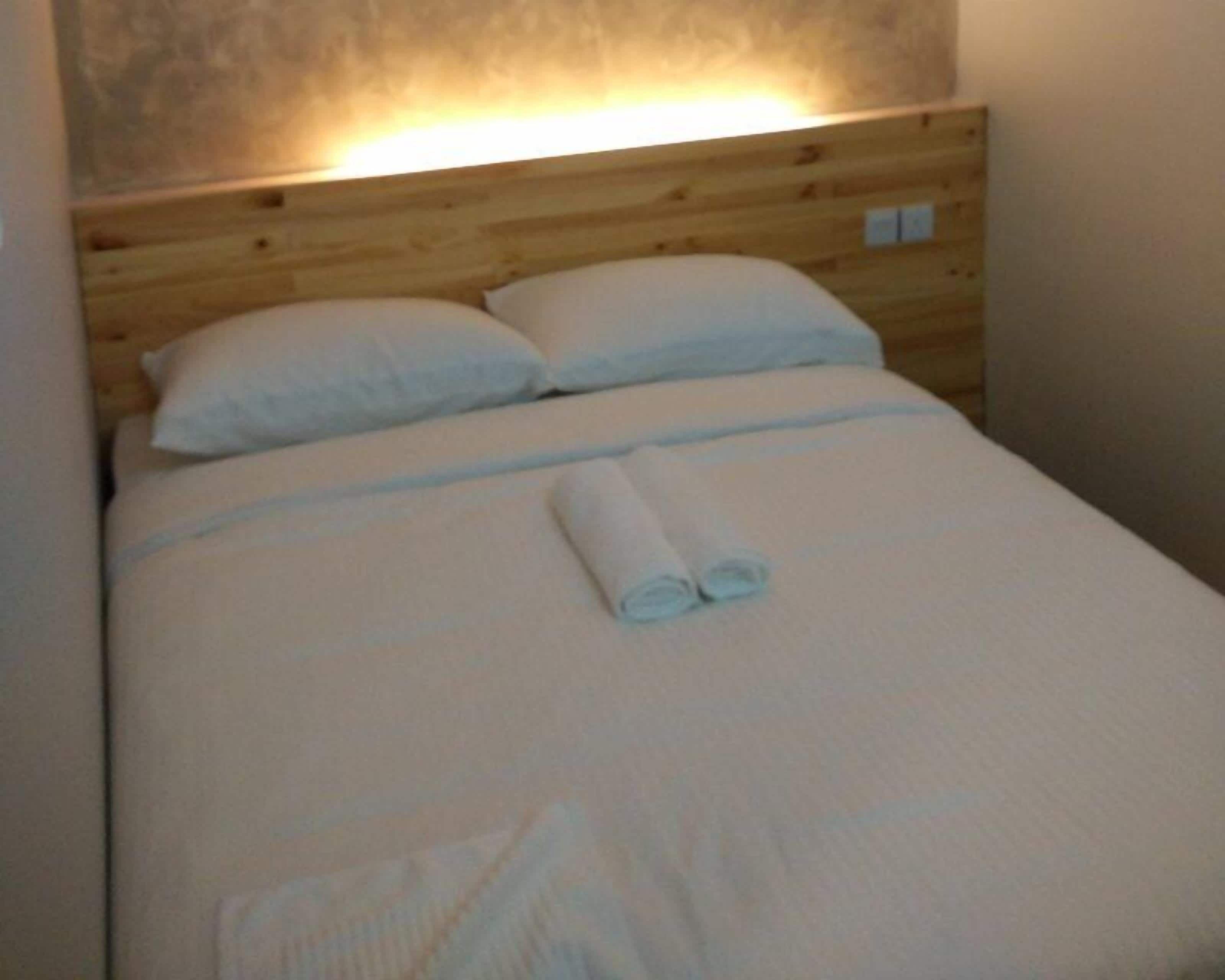 A neatly made bed with white linens and a rolled towel in the center.