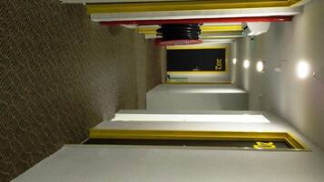 A narrow corridor with yellow safety markings, a fire extinguisher, and a fire exit sign.
