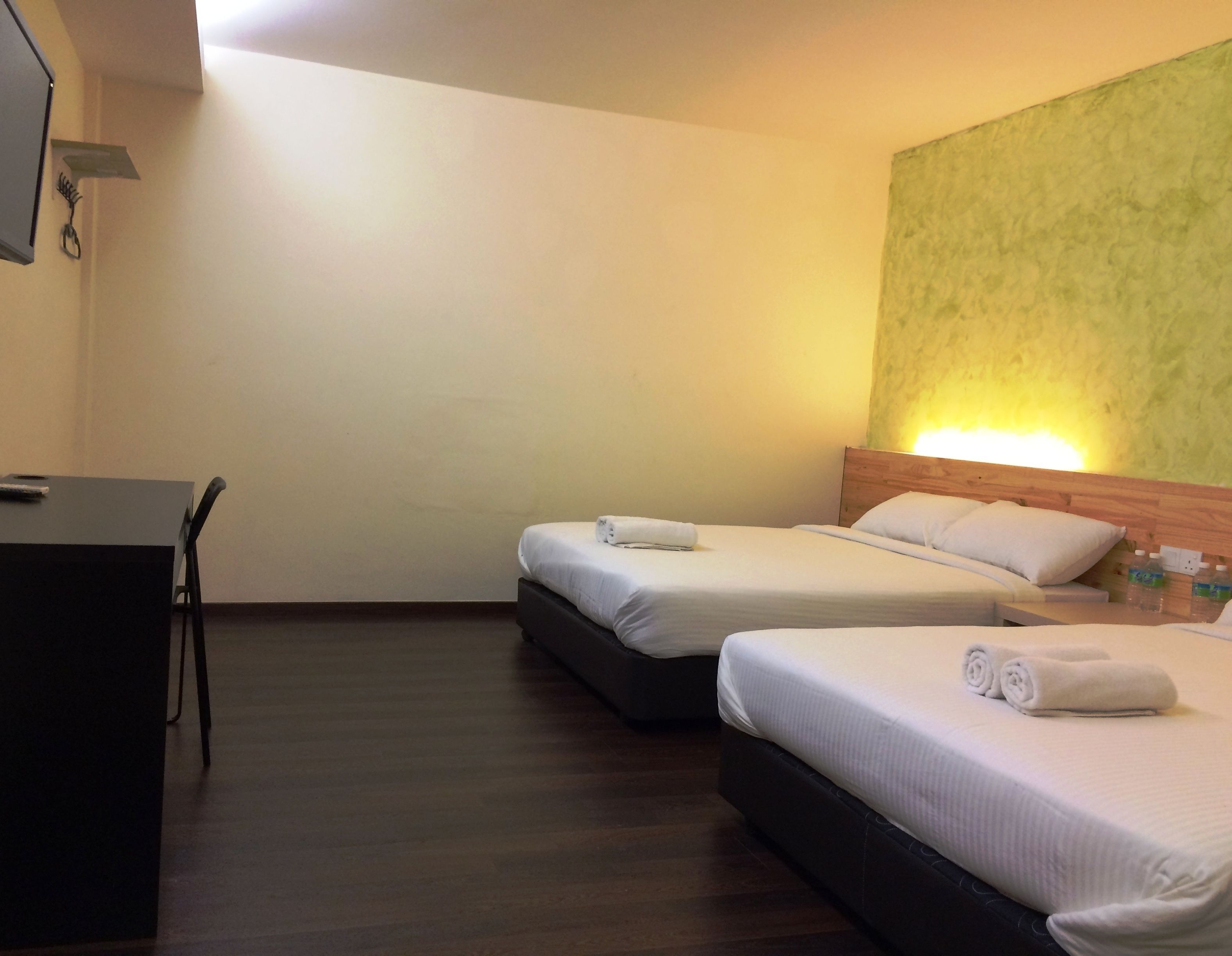 Una habitación de hotel con dos camas, un escritorio y una pared verde con textura.