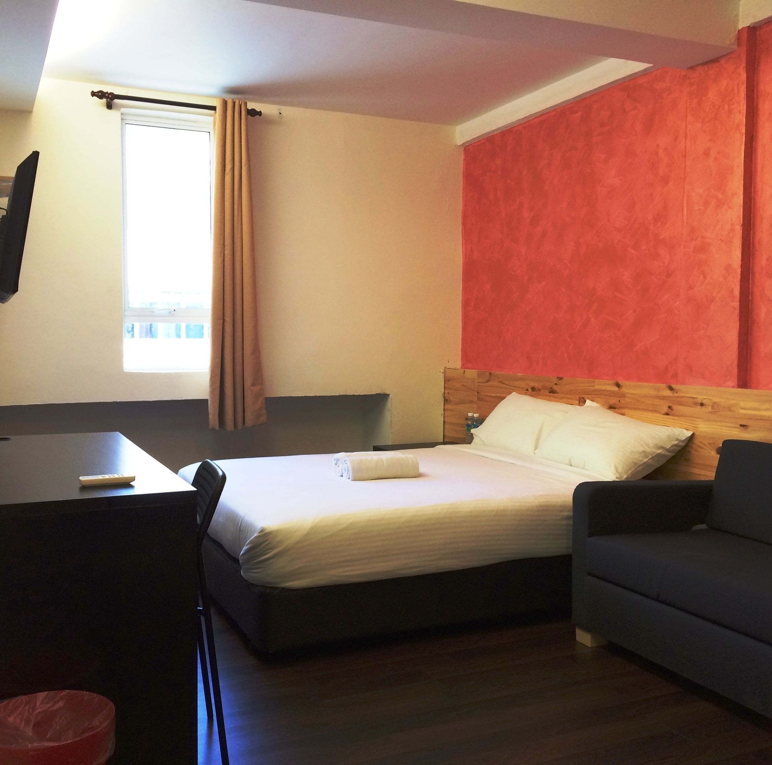 Une chambre d’hôtel avec un lit, un bureau, une chaise, un canapé et une fenêtre avec des rideaux.