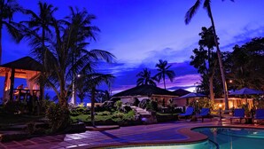 A nighttime resort pool area with clear water, palm trees, and a moon in the sky. - Blue Star Dive & Resort (Anda)