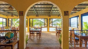 A restaurant with a tropical view, featuring wooden tables and chairs, a globe on a table, and a sun decoration on the ceiling. - Blue Star Dive & Resort (Anda)