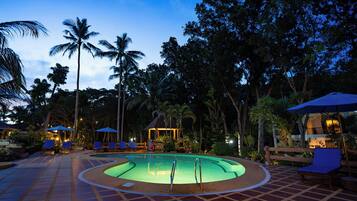 A pool area with lounge chairs and umbrellas, surrounded by palm trees and a gazebo.
