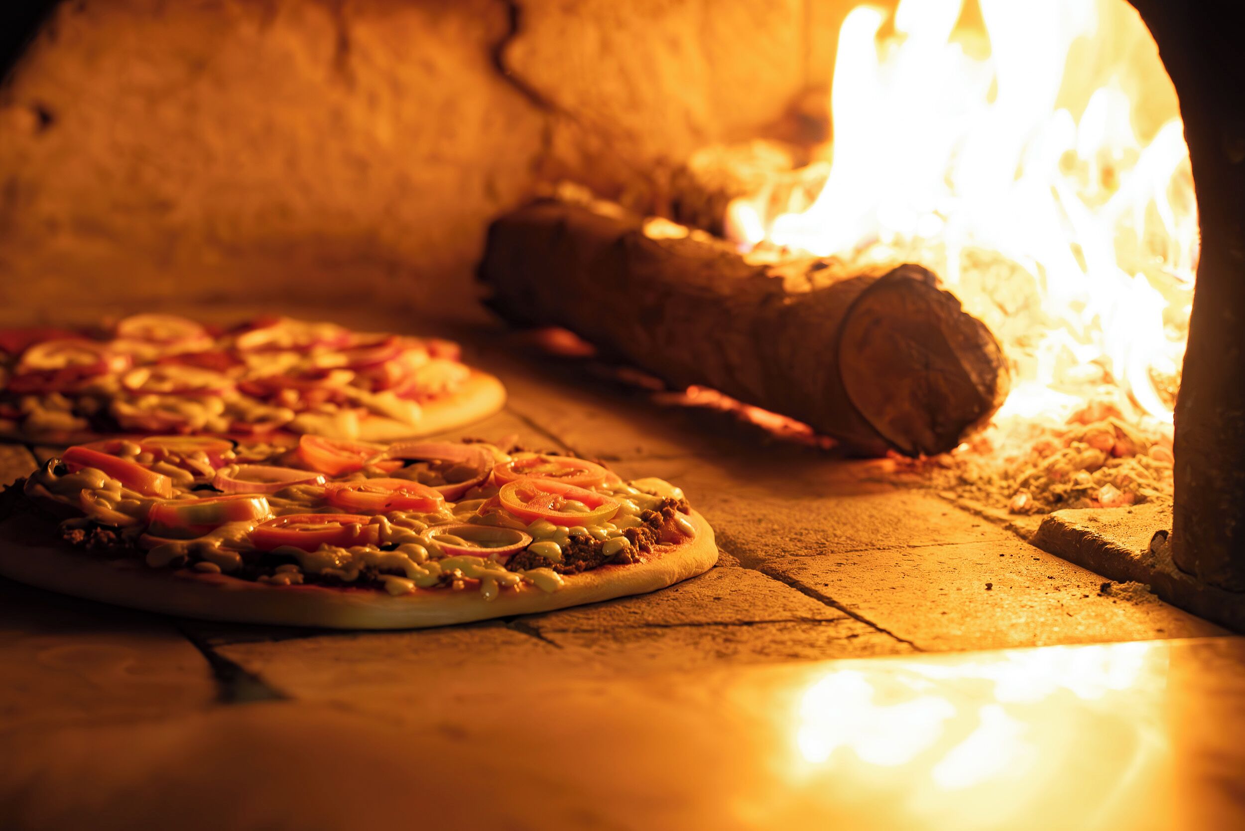 Dos pizzas horneándose en un horno de leña.