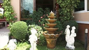A garden with a tiered water fountain, a spherical hedge, and two white statues. - Baanmalai Hotel Chiangrai (Chiang Rai)